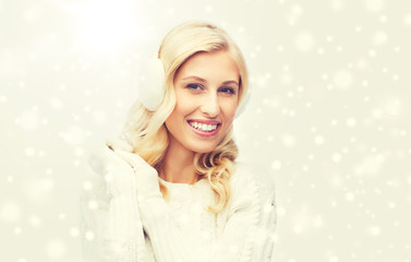 smiling young woman in winter earmuffs and sweater
