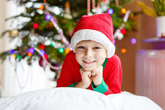 Little kid boy in santa hat with Christmas tree and lights on background.