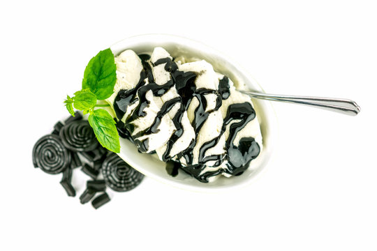 A green bowl with delicious vanilla ice cream, licorice sauce topping and mint. Licorice candy on the side. Selective focus from above.