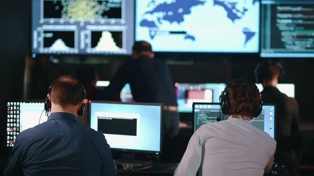 A team of security personnel working in a busy system control room, could be a weather station airport traffic control. It could be a power station or police army control facility.