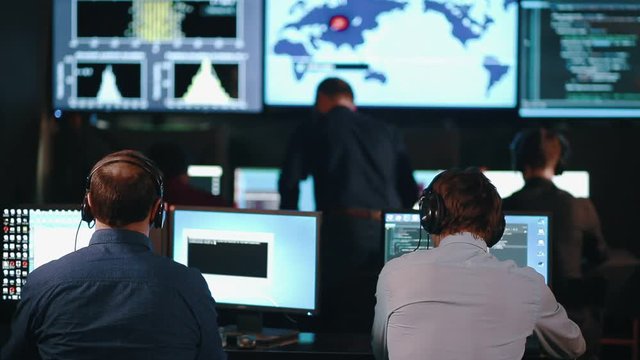 A team of security personnel working in a busy system control room, could be a weather station airport traffic control. It could be a power station or police army control facility.