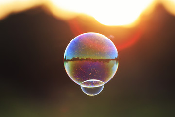 beautiful iridescent soap bubble with reflection landscape flies to sunset over summer meadow