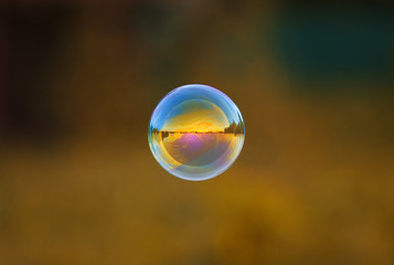round iridescent soap bubble flying over the Sunny meadow with the mirrored landscape