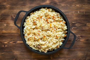 The pilaf. Rice cooked with vegetables and meat. In a cast iron dish on a wooden background.