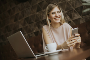 young woman sitting in cafe, drinking coffee and surf the internet with a smile
