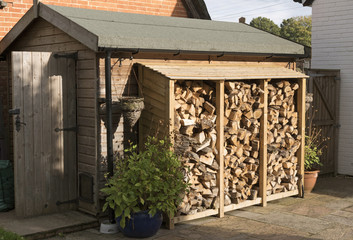 Log store standing against a garden shed