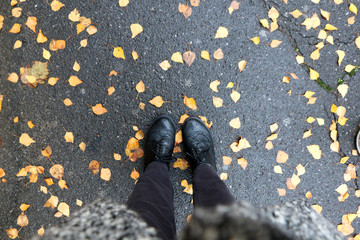 Unrecognizable person wearing gray clothes and black Oxford shoes. Fallen yellow leaves on the...