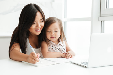 Smiling young asian woman sitting with her little daughter