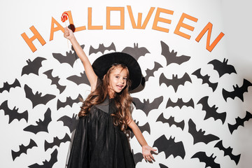 Happy little girl dressed in halloween costume holding lollipop