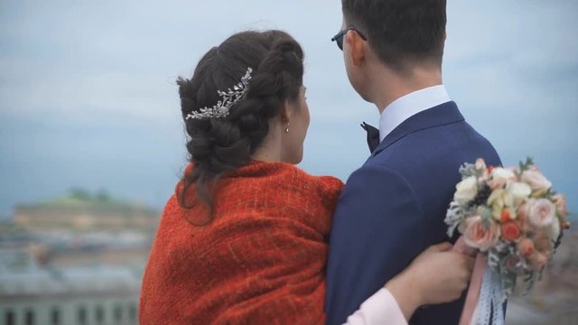 Couple standing on the roof. Happy bride and groom looking to the city from high altitude. Back niddle view