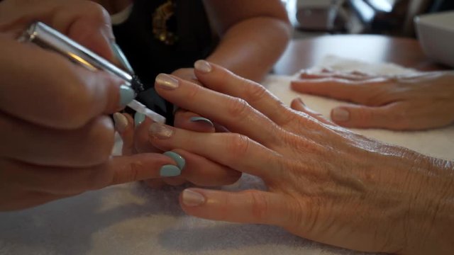 Tight shot of manicurist painting on salmon colored polish onto the nails of a caucasian woman.