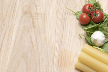 Dried cannelloni pasta with tomato and spinach leaves on a wooden background 