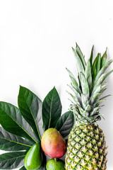 Tropical fruits background. Mango near exotic leaf and pineapple on white top view copyspace