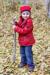 Portrait of a happy joyful child in a hat and a red jacket, jeans against a background of autumn forest and yellow leaves
