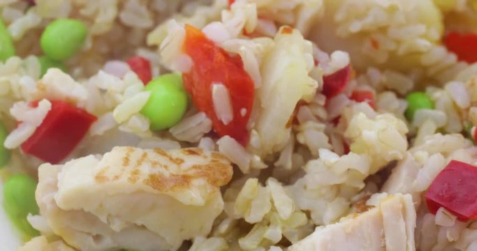 Close video of mixing chicken, rice, water chestnuts, red peppers and pineapple chunks to a sauce in a plastic bowl with a fork.