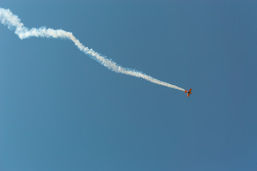 Aerobatic plane  leaving a white smoke trail in the blue sky.