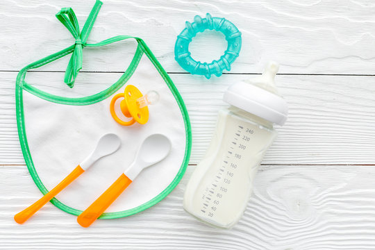 bottle with breastmilk and infant formula powdered healthy food, toys and bib on wooden background top view