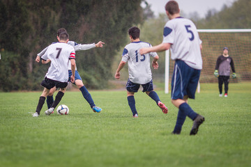 Obraz na płótnie Canvas Young men playing soccer in the rain on a grass field