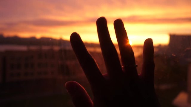 Women hand touches the sun by the window on sunset city background in slow motion. 3840x2160