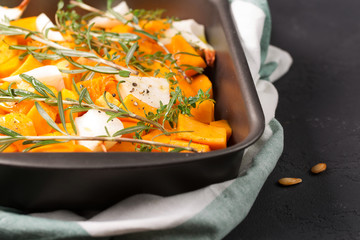 A bowl with pumpkin for baking with onions, olive oil, rosemary and thyme, pumpkin, horizontal, selective focus, black background

