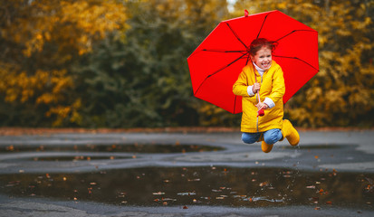happy child girl with an umbrella and rubber boots in puddle  on autumn walk
