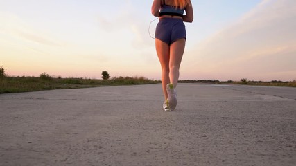 young woman runs and listens to music on headphones on a summer afternoon at sunset, back view