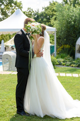 Happy bride and groom with bridal bouquet  kissing in park on summer wedding day. Kissing wedding...