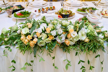 Lush floral arrangement of white and orange fresh flowers and greenery on wedding table for newlyweds. Beautiful flowers on table with white cloth, free space. Luxury wedding table decorations