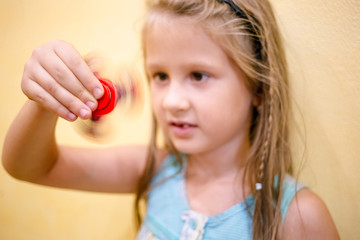 Little girl playing with red fidget spinner toy to relieve stress at home