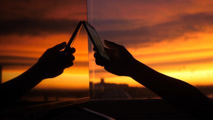 Female hand uses smart phone on a city background of sunset in the reflection of the window.