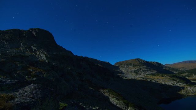 Night Stars time lapse above mountain lake and peaks, Moving full moon and shadow