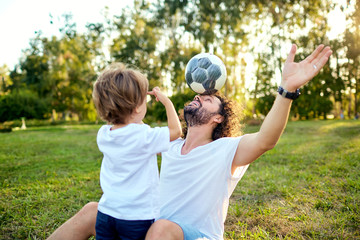 Father son playing with a ball on the grass in the park. Father's Day.