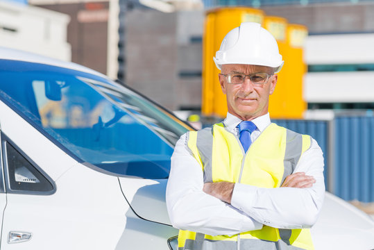 Senior builder man outdoors at construction site near his car looking in camera
