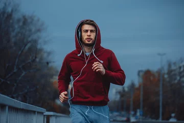 Tuinposter Man in red hoodie jogging beside the road in the city © djile