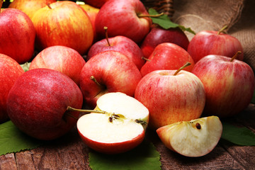 Ripe red apples with leaves on wooden background