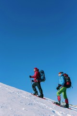 Climber with backpack trekking poles snowshoes rises to the top of the mountain in the snow on a background of beautiful blue sky.
