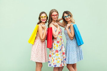 Young adult pretty womans with glasses, casual new dress with long brunette and blonde curly hair posing on green background, holds colorful shopping packages or bags