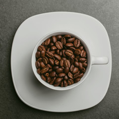 White coffee cup filled with coffee seeds on black surface background.