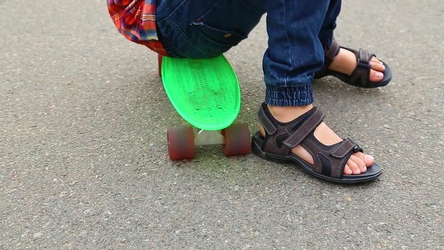 Closeup of male feet of child resting on green plastic roller skate on pavement in city. White kid of 10 years has fun in city park on warm summer or autumn day. Real time full hd video footage.