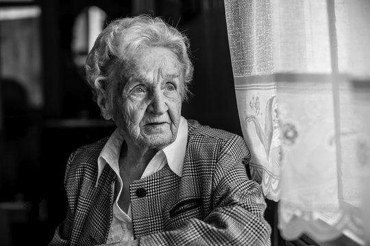 Portrait of stern old women, black and white near the window.