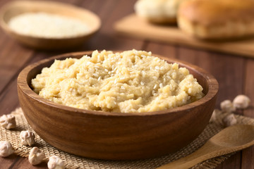 Chickpea spread or hummus with sesame seeds in wooden bowl, photographed with natural light (Selective Focus, Focus one third into the chickpea spread)