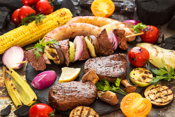 Assorted delicious grilled barbecue meat with vegetable. Beef grilled steaks with spicy sausages, beef kebabs, corn, cherry tomato,  pepper, slices of onion, zucchini, eggplant.