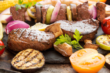 Assorted delicious grilled barbecue meat with vegetable. Beef grilled steaks with spicy sausages, beef kebabs, corn, cherry tomato,  pepper, slices of onion, zucchini, eggplant.
