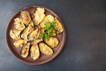 Mussels baked with cheese and spices in shell mussels. Lemon, parsley and spices around plate on dark background.