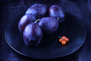 Blue plums and orange rowan berries on a black plate for designer