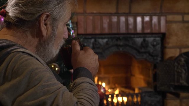 Senior man eating cookie and drinking tea near the fireplace at Christmas eve