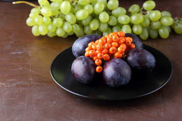 Green grapes, blue plums and orange rowan berries on a black plate for designer in retro style