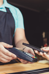 Person paying pay through smartphone using NFC technology in outdoor cafe