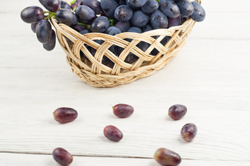 Lot of scattered grapes beside full wicker basket of fresh ripe blue grapes on old wooden rustic white planks