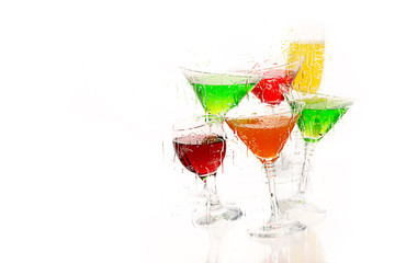 Seven cocktail  and wine glasses with color drinks in the chaotic movement stand on the reflecting surface.